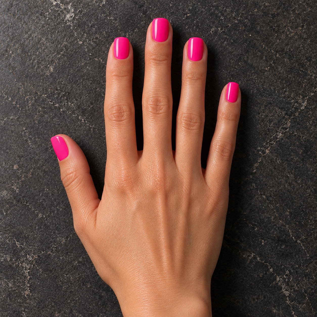 Glossy vivid pink Fever nails resting on matte charcoal stone